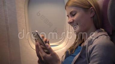 飞机窗户附近美丽迷人的女人。 长途飞行。 使用智能手机，浏览